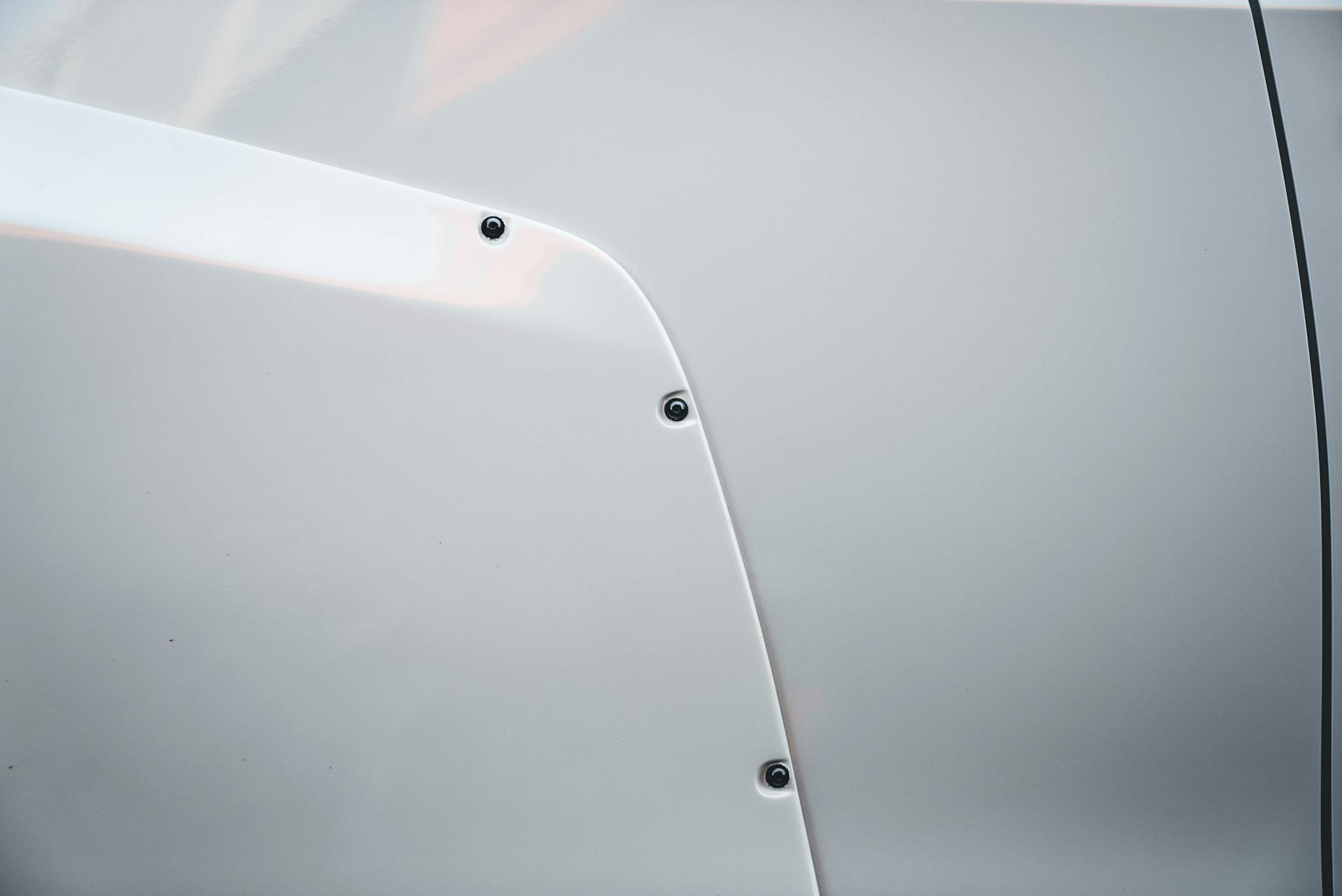 Detailed view of a white car's panel highlighting screws and smooth textures.